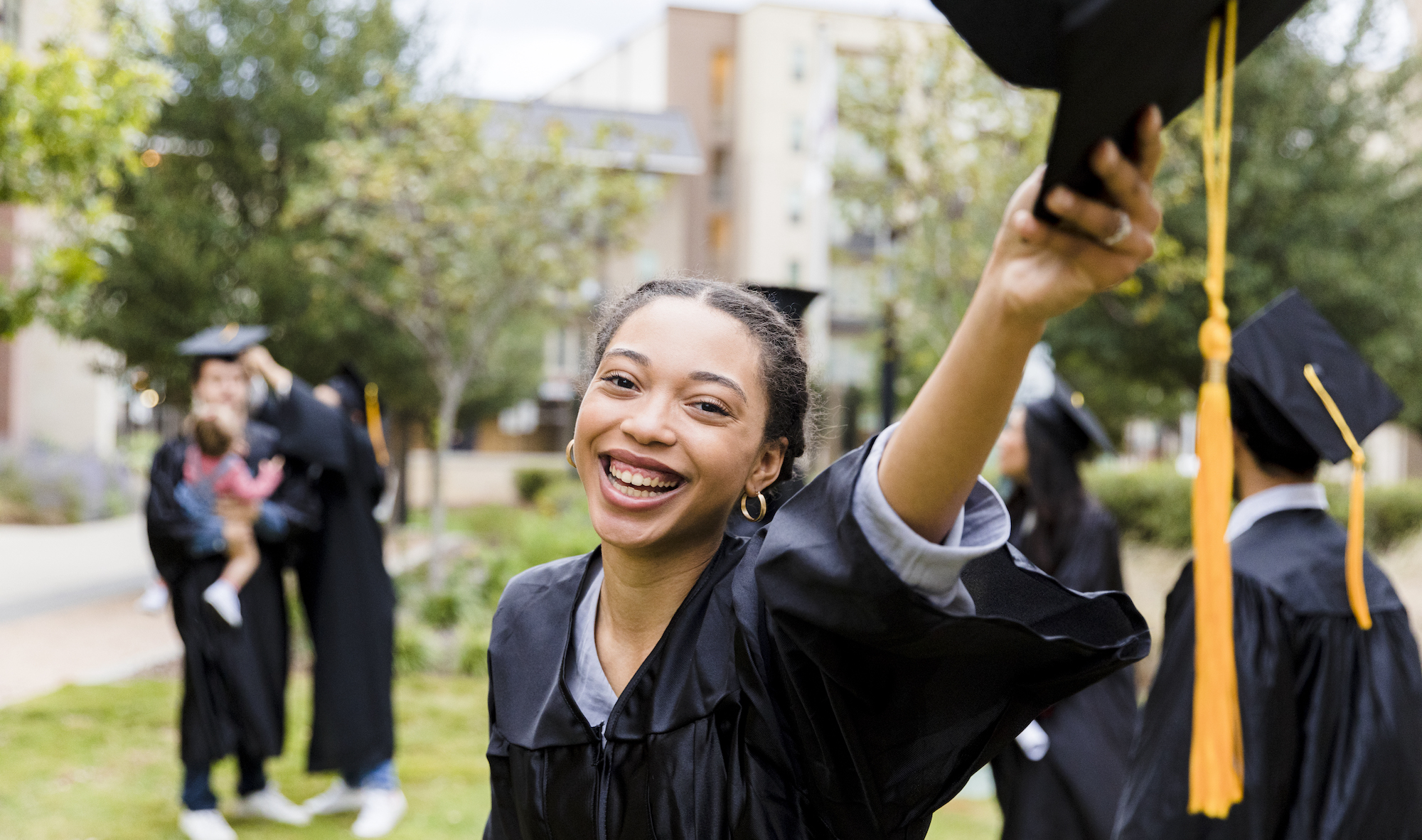 Life insurance for college graduates A young female graduate smiles at the camera while holding her mortarboard