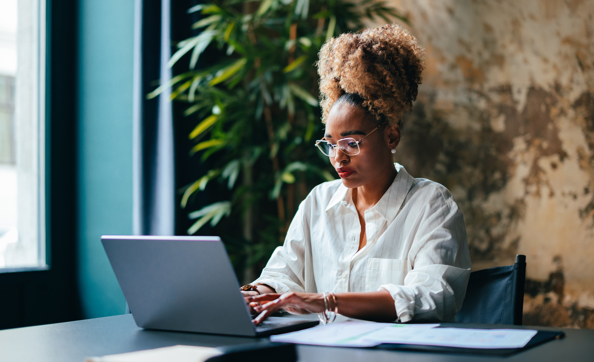 Entrepreneur using laptop at desk A young black female entrepreneur uses a laptop at a desk with papers spread out